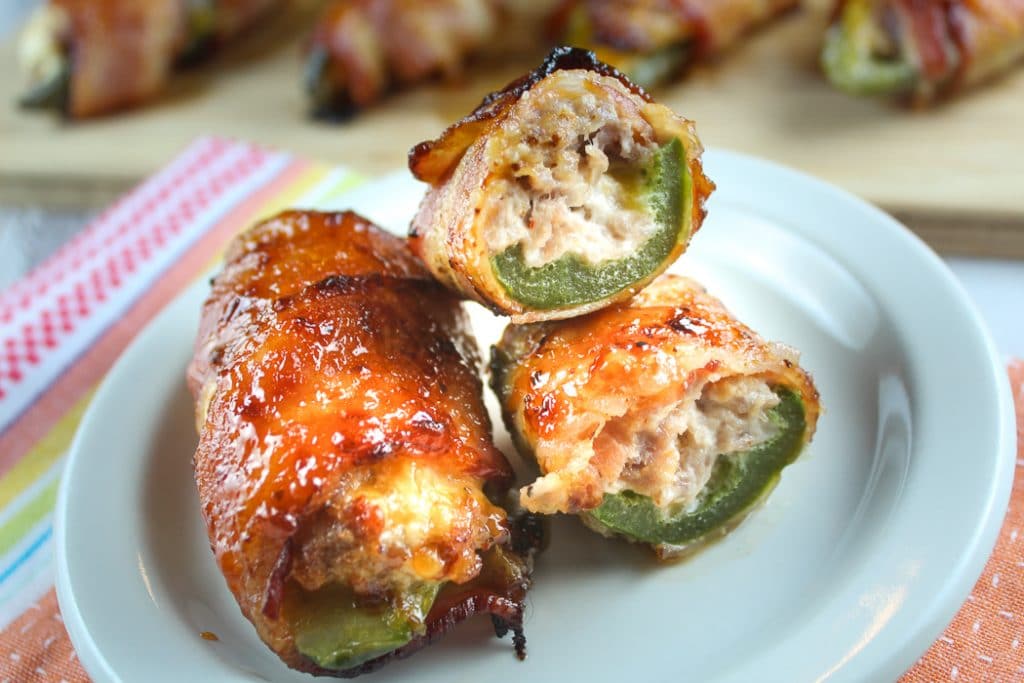 These Sausage Stuffed Jalapenos wrapped in bacon are finger lickin', lip smackin' good! Jalapeno peppers filled with sausage, cream cheese and CoJack cheese - then wrap it in bacon - I promise you're going to eat them ALL!!!!!
