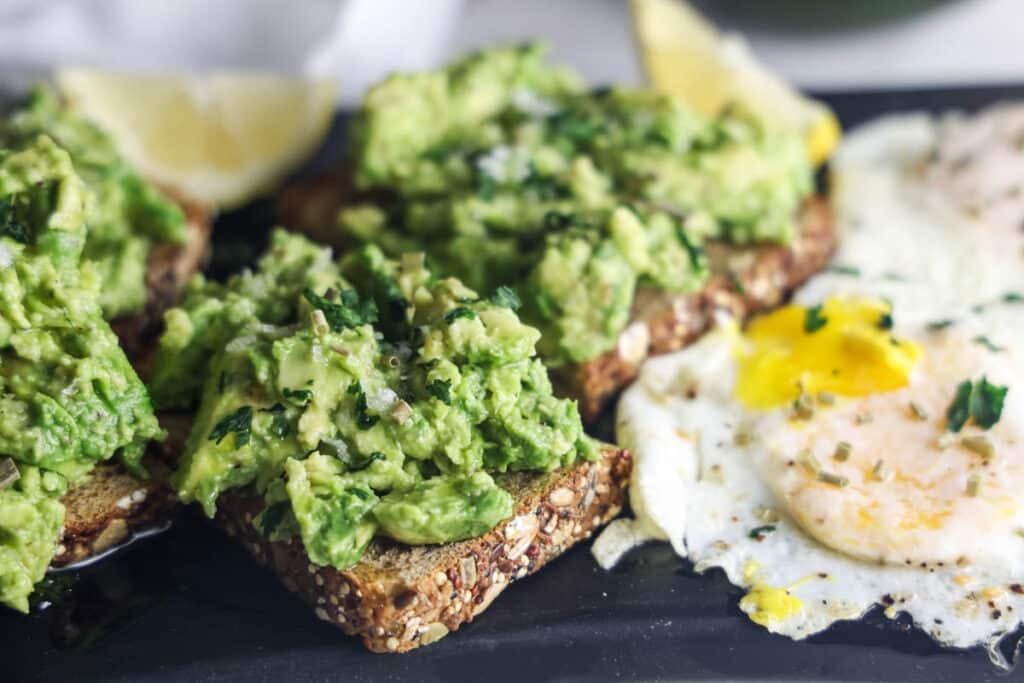 Copycat First Watch Avocado Toast made with thick-cut whole grain toast, smashed avocado, lemon, extra virgin olive oil and flaky sea salt, served with two basted eggs.