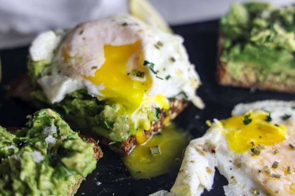 Copycat First Watch Avocado Toast made with thick-cut whole grain toast, smashed avocado, lemon, extra virgin olive oil and flaky sea salt, served with two basted eggs.