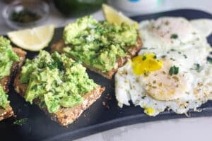 Copycat First Watch Avocado Toast made with thick-cut whole grain toast, smashed avocado, lemon, extra virgin olive oil and flaky sea salt, served with two basted eggs.