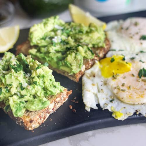 Copycat First Watch Avocado Toast made with thick-cut whole grain toast, smashed avocado, lemon, extra virgin olive oil and flaky sea salt, served with two basted eggs.