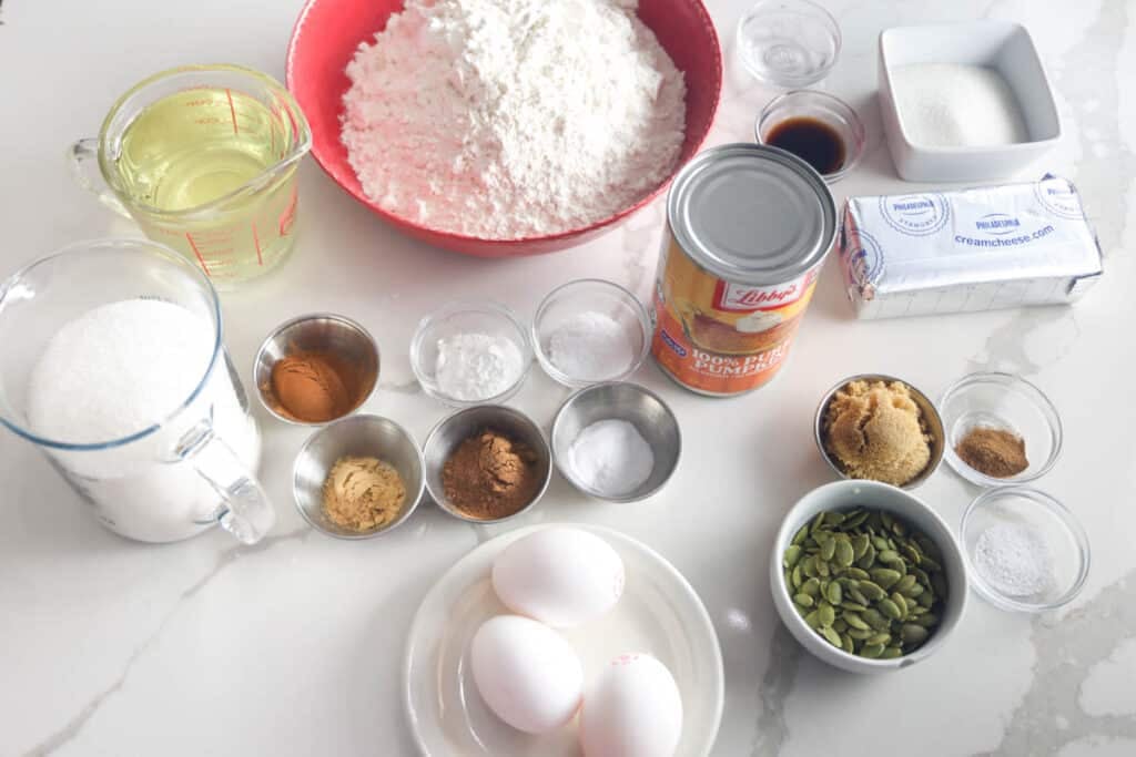 Ingredients for pumpkin cream cheese muffins, including pumpkin puree, cream cheese, flour, sugar, eggs, oil, spices and pumpkin seeds.