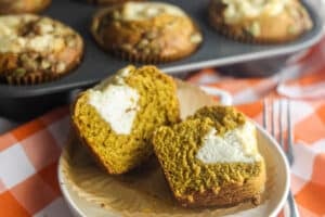 A homemade pumpkin cream cheese muffin cut in half, showing the soft spiced crumb and creamy cheesecake center.