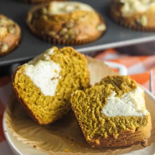 A homemade pumpkin cream cheese muffin cut in half, showing the soft spiced crumb and creamy cheesecake center.