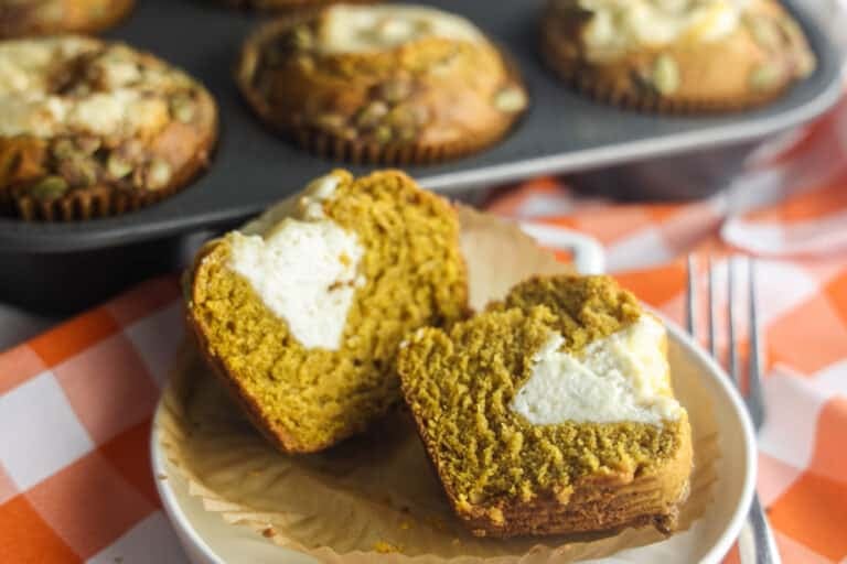 A homemade pumpkin cream cheese muffin cut in half, showing the soft spiced crumb and creamy cheesecake center.