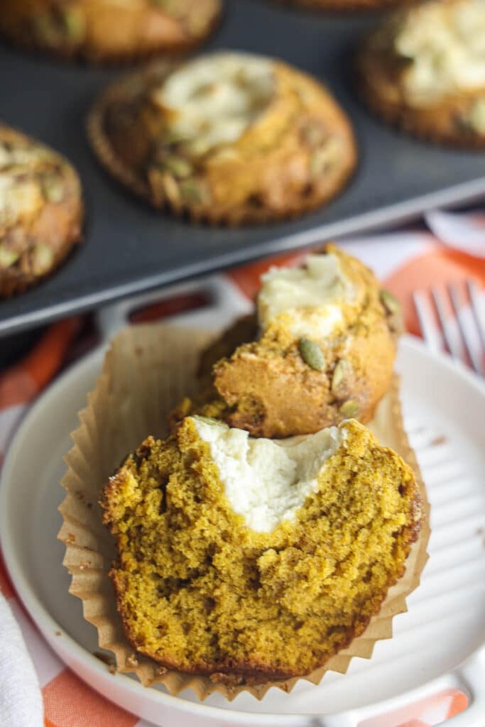 A homemade pumpkin cream cheese muffin cut in half, showing the soft spiced crumb and creamy cheesecake center.